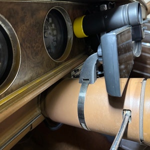 Puede incluir: Primer plano del interior de un coche con un salpicadero marrón, un volante negro y un dispositivo negro y amarillo montado en el salpicadero. Un destornillador es visible en la esquina inferior derecha de la imagen.