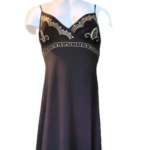 May include: A black sleeveless dress with gold and silver embellishments. The dress has a V-neckline and a fitted bodice. The skirt is flowy and falls to the floor.