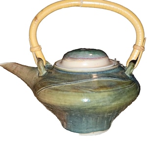 May include: A handcrafted ceramic teapot with a bamboo handle. The teapot features a rounded body with a spout and a lid. The colors are shades of green, blue, and brown, with a cream-colored lid. The handle is made of light brown bamboo.