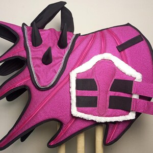 A pink horse saddle pad with black trim and a black and white horse leg wrap. The saddle pad has a dragon design with spikes and the leg wrap has a white fleece lining.