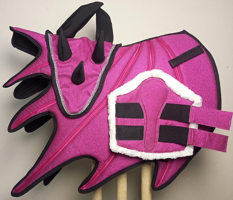 A pink horse saddle pad with black trim and a black and white horse leg wrap. The saddle pad has a dragon design with spikes and the leg wrap has a white fleece lining.