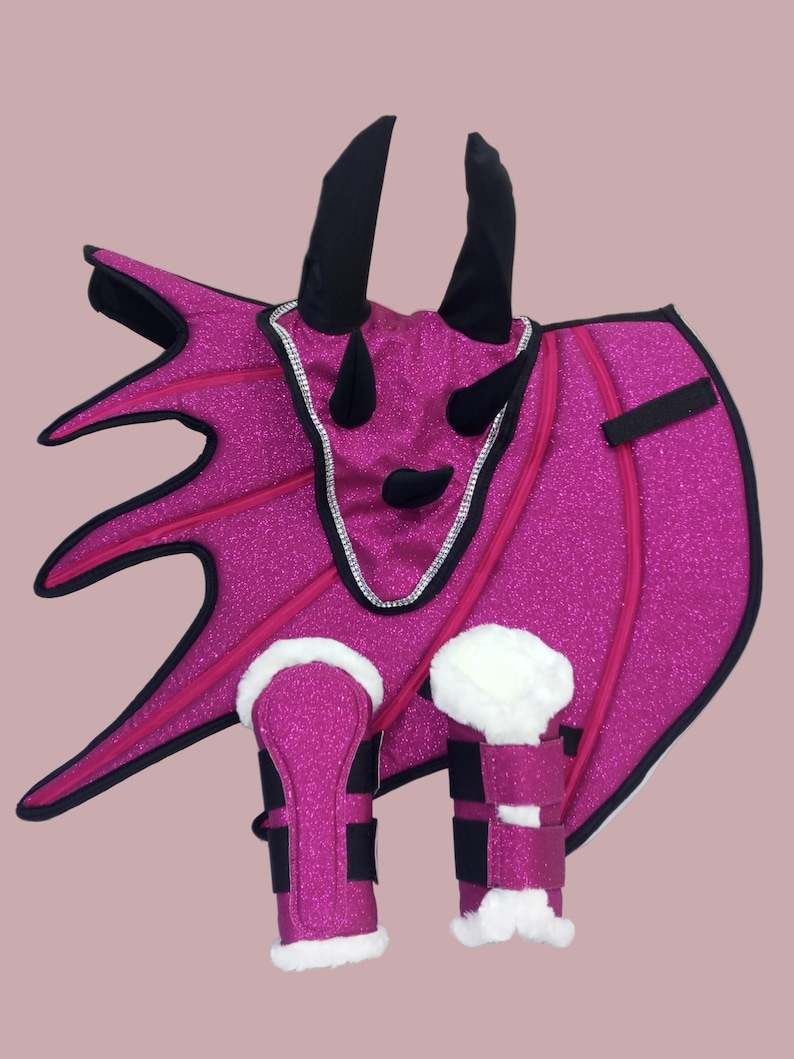 May include: A bright pink dragon costume set with glittery fabric, black horns, and white faux fur trim. The set includes a wing piece, headpiece, and leg warmers, perfect for a costume party or imaginative play.
