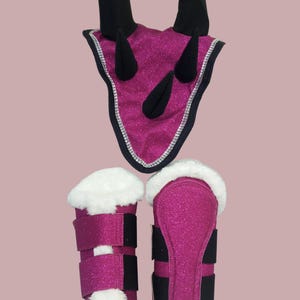May include: A set of equestrian equipment in a vibrant fuchsia glitter fabric. The set includes a headstall with black horns and a silver trim, along with matching leg wraps featuring white faux fur and black straps. The items are designed for horse riding.