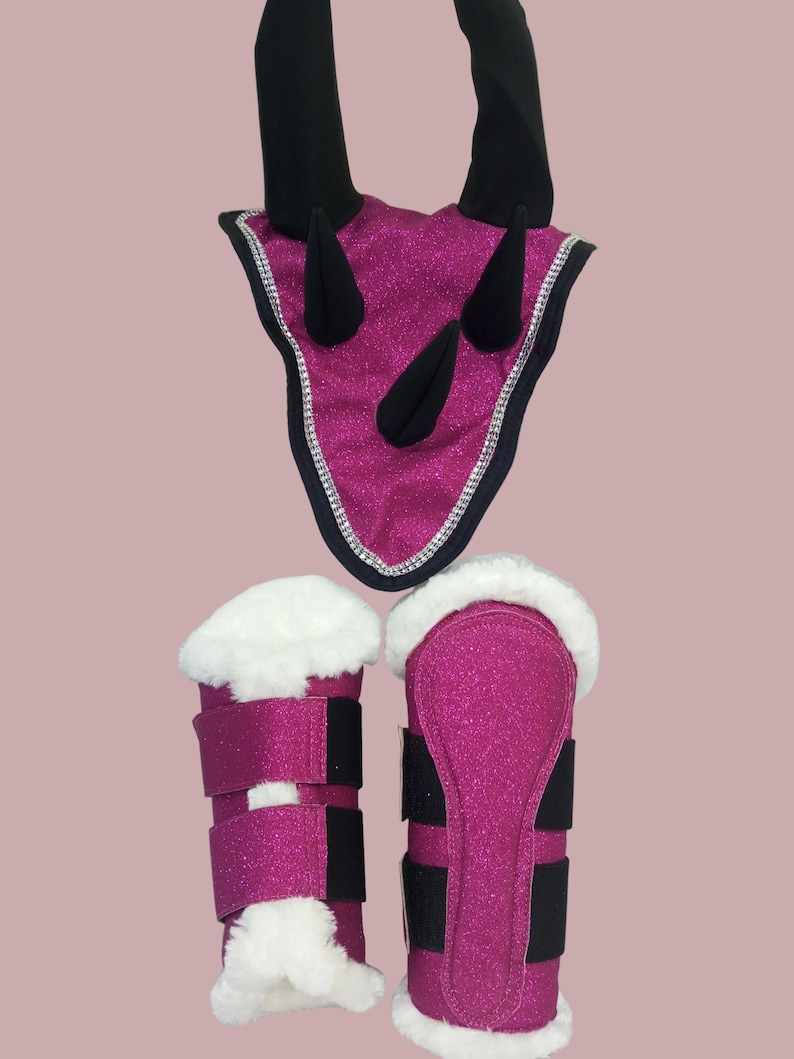 May include: A set of equestrian equipment in a vibrant fuchsia glitter fabric. The set includes a headstall with black horns and a silver trim, along with matching leg wraps featuring white faux fur and black straps. The items are designed for horse riding.