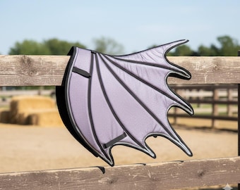 May include: A gray dragon wing prop with black trim and straps, resting on a wooden fence. The wing has a textured surface and a curved, pointed shape, suggesting a fantasy or costume theme.