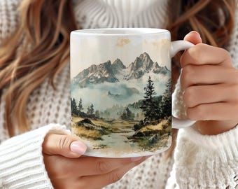 May include: White ceramic mug with a scenic mountain landscape design. The image features a misty mountain range with a river flowing through a valley. The mountains are painted in shades of blue, green, and brown.