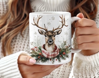 May include: White ceramic mug with a winter scene featuring a deer wearing a red and black plaid scarf. The deer is surrounded by green pine branches and red berries. The background is white with snowflakes.