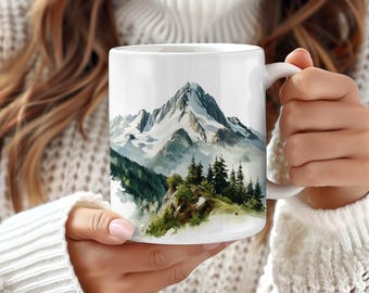 May include: White ceramic mug with a watercolor illustration of a snow-capped mountain range with green trees and fog.
