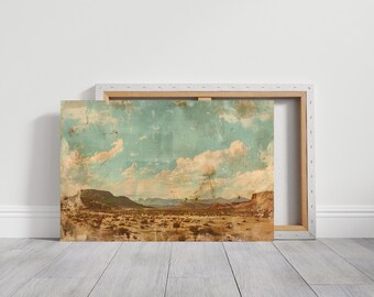 May include: A canvas print of a desert landscape with mountains, shrubs, and a cloudy sky. The artwork has a vintage, distressed look with a light blue sky and tan and brown tones. The canvas is mounted on a wooden frame.
