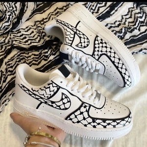 May include: White leather sneakers with a black and white geometric pattern on the sides and swoosh. The pattern resembles a traditional Palestinian keffiyeh.