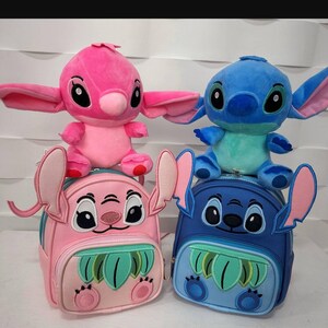 Può includere: Due zaini Stitch di peluche, uno rosa e uno blu. Ogni zaino presenta un personaggio Stitch di peluche in cima. Gli zaini hanno un design a foglia verde sul davanti.