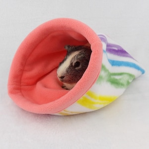 May include: A pink and white striped fleece guinea pig bed with a guinea pig inside.