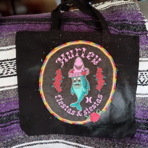 May include: Black tote bag with a colorful circular design featuring a cartoon shark wearing a pink sombrero. The design includes the text "Hurley", "Fiestas", and "Siestas".