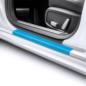 May include: A vibrant blue car door sill protector fitted to a white car. The protector is rectangular and runs along the bottom edge of the door frame. The car's interior, including the seat and controls, is visible.