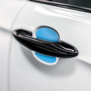 Könnte beinhalten: Nahaufnahme eines Autotürgriffs. Der Griff ist schwarz und glänzend, mit einem geschwungenen Design. Die Tür ist weiß und der Griff hat einen hellblauen Akzent. Der Griff ist horizontal positioniert.