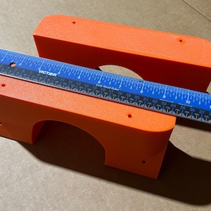 May include: Two bright orange plastic pieces with a rounded archway cut out. The pieces are stacked on top of each other and a blue ruler is placed on top of them. The ruler is marked with inches and has the word "VICTOR" printed on it.