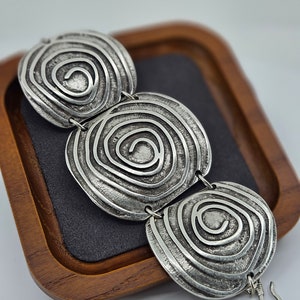 May include: Silver bracelet with three connected oval-shaped links. Each link features a raised, textured design of concentric circles.