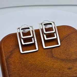 May include: A pair of silver earrings with a geometric design. Each earring features two overlapping square shapes.