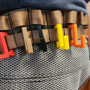 May include: A brown tactical belt with multiple loops and a variety of colored plastic hooks attached to the loops. The hooks are red, orange, yellow, and black.