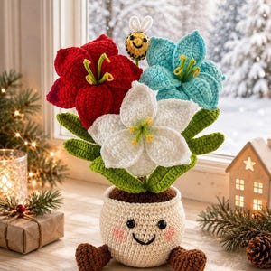 Op de afbeelding: Een gehaakte potplant met drie grote bloemen in rood, wit en lichtblauw met groene bladeren. De crèmekleurige pot heeft een lachend gezicht met zwarte ogen, een geborduurde mond en roze wangen, met twee bruine voetjes aan de onderkant.
