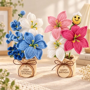 Könnte beinhalten: Zwei gehäkelte Blumenarrangements in beigen Töpfen. Der linke Topf hat ein Holzschild mit der Aufschrift KEEP GROWING STRONG und zeigt blaue und weiße Lilien. Der rechte Topf trägt die Aufschrift HAPPY BIRTHDAY und zeigt rosa und weiße Lilien sowie eine kleine Biene.
