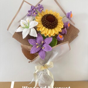 May include: A wrapped bouquet of crocheted flowers, including a large yellow sunflower, white lilies, and purple blooms. The bouquet is wrapped in brown and white paper and tied with a cream ribbon. The text "- Wrapped bouquet" is visible.