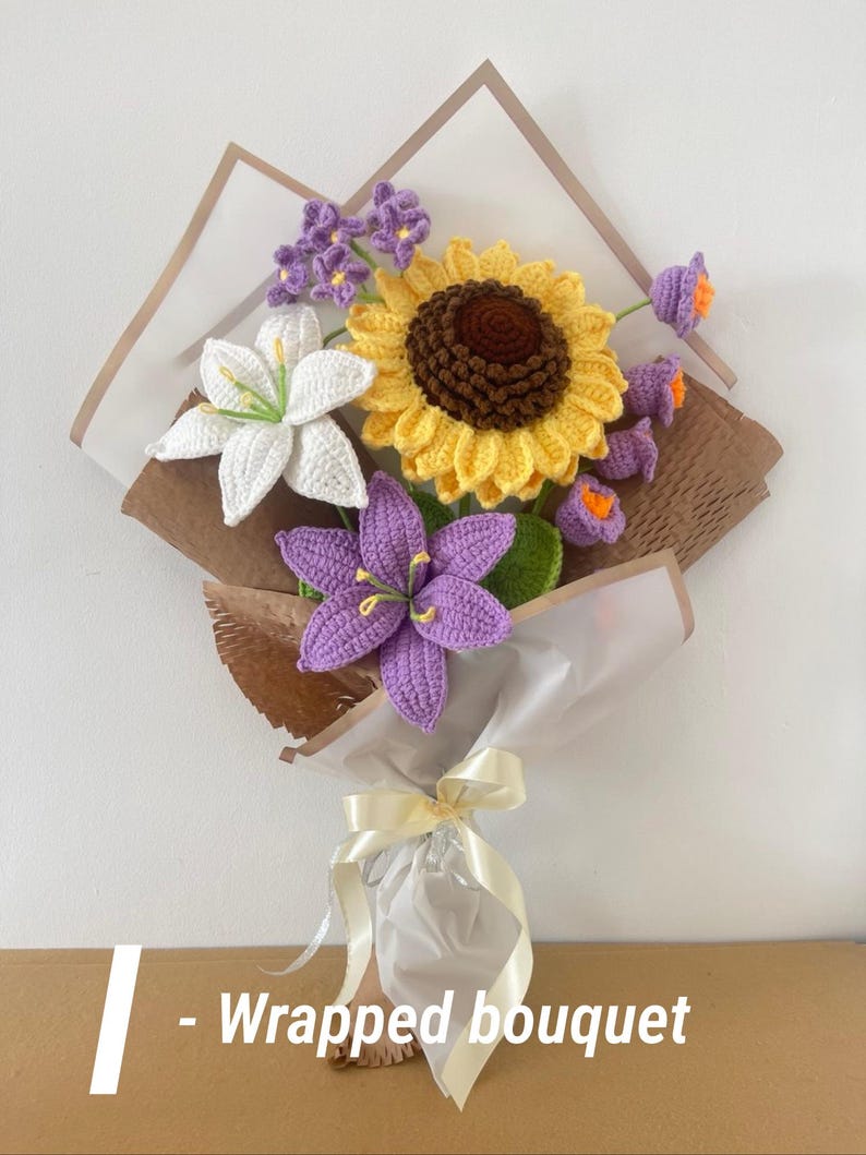 May include: A wrapped bouquet of crocheted flowers, including a large yellow sunflower, white lilies, and purple blooms. The bouquet is wrapped in brown and white paper and tied with a cream ribbon. The text "- Wrapped bouquet" is visible.
