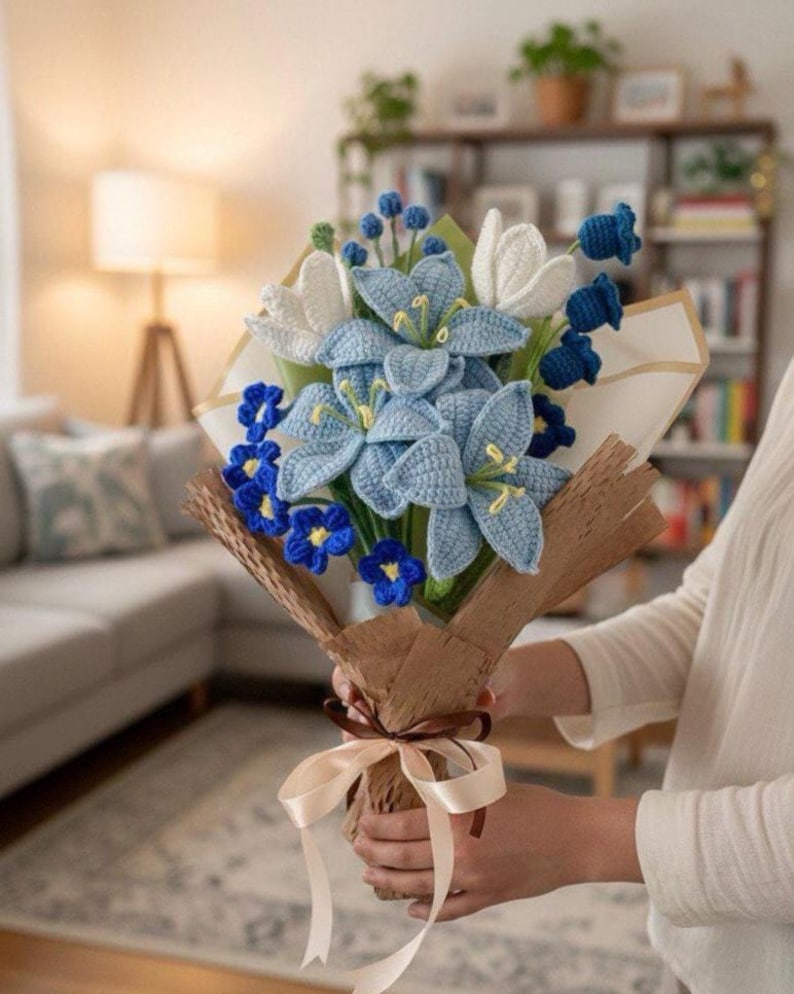 May include: A handcrafted bouquet of crocheted flowers in shades of blue, white, and yellow. The bouquet includes lilies, tulips, and smaller blue flowers, wrapped in brown paper and tied with a cream ribbon. A unique, handmade gift.
