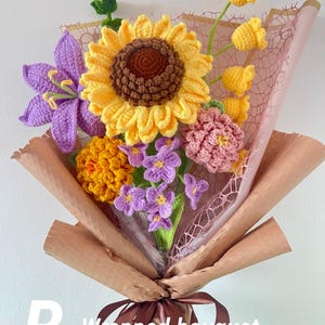 May include: A handmade crochet bouquet featuring a large yellow sunflower, purple lily, and other colorful flowers. The bouquet is wrapped in brown paper and tied with a brown ribbon. The text "B - Wrapped bouquet" is visible.