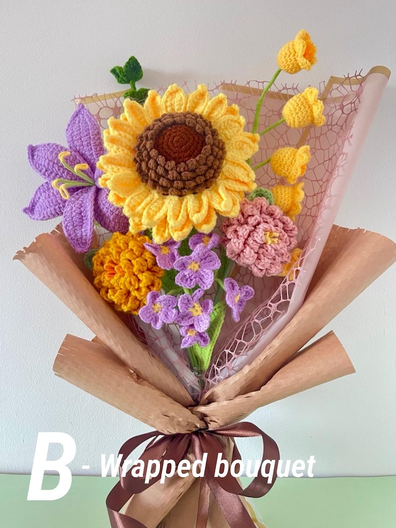 May include: A handmade crochet bouquet featuring a large yellow sunflower, purple lily, and other colorful flowers. The bouquet is wrapped in brown paper and tied with a brown ribbon. The text "B - Wrapped bouquet" is visible.