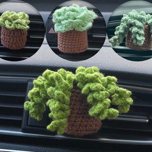Könnte beinhalten: Drei gehäkelte grüne Pflanzen-Lufterfrischer in braunen Töpfen, die an den Lüftungsschlitzen eines Autos hängen.