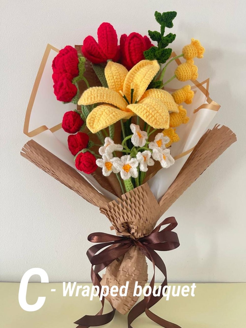 May include: A handcrafted crochet bouquet featuring red tulips, yellow lilies, and small white flowers. The bouquet is wrapped in brown paper and tied with a brown ribbon. The text "C - Wrapped bouquet" is visible.