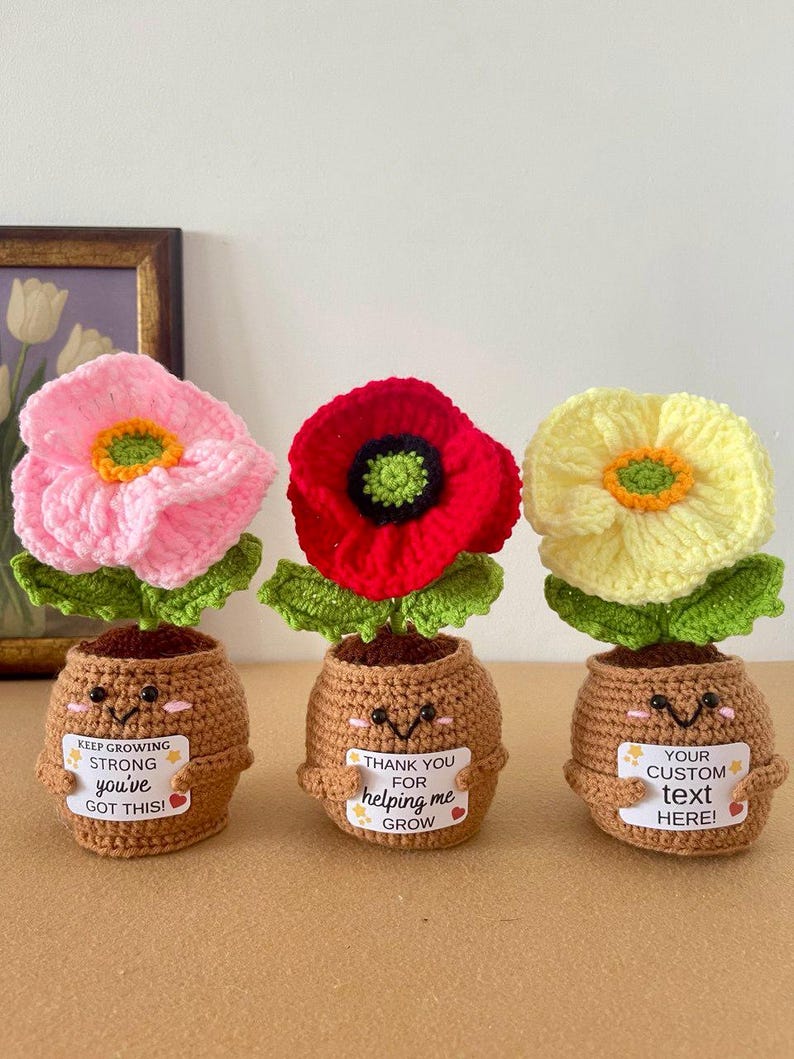 May include: Three crocheted potted flowers in pink, red, and yellow with green leaves. Each brown pot has a smiling face and holds a white sign. The signs read: KEEP GROWING STRONG you've GOT THIS!, THANK YOU FOR helping me GROW, and YOUR CUSTOM text HERE!