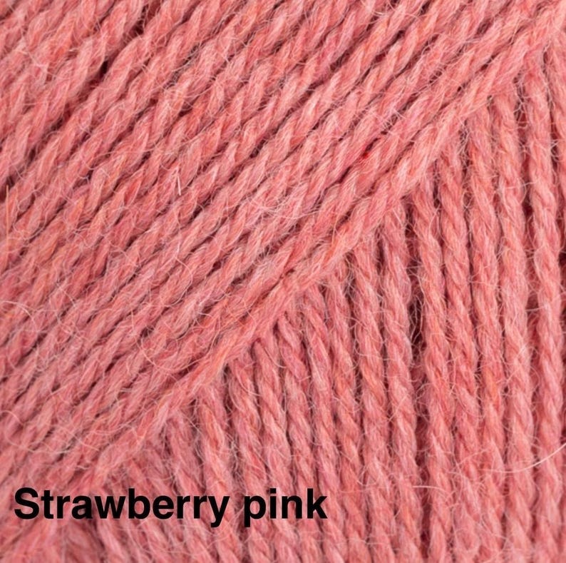 May include: A close-up view of a skein of yarn in a solid strawberry pink colour. The yarn features a multi-ply twisted texture with a soft, slightly fuzzy appearance. The text "Strawberry pink" is printed in black at the bottom left corner.