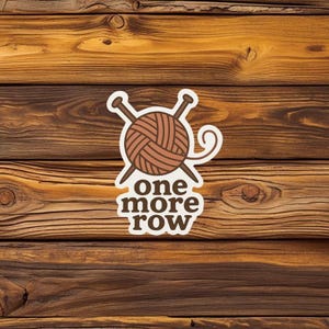 May include: A sticker featuring a brown yarn ball with two crossed knitting needles. The text "one more row" is below the yarn ball in brown. The sticker is set against a wooden background.