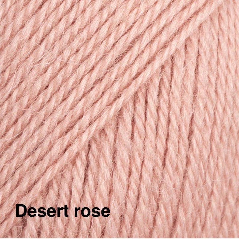 May include: A close-up view of soft, light pink yarn with a visible twisted fibre texture. The yarn is arranged in parallel vertical strands. The text 'Desert rose' is printed in black in the bottom left corner of the image.