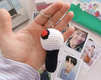 May include: White crocheted keychain shaped like a light stick with a black handle and a red circle on the top. The keychain is attached to a silver key ring.