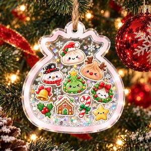 Puede incluir: Un adorno navideño transparente en forma de bolsa, relleno de purpurina holográfica y pequeños iconos festivos que incluyen un muñeco de nieve, una casa de jengibre, un bastón de caramelo, una estrella, una campana, acebo y varios personajes de dumplings sonrientes.