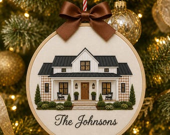 May include: A round embroidery hoop ornament featuring a fabric-stitched illustration of a white farmhouse with a black roof, a front porch, and two chairs. A brown satin bow sits at the top, and the text The Johnsons is printed in black script.