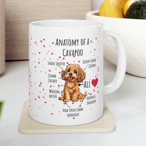 Könnte beinhalten: Eine weiße Keramiktasse mit einer Cartoon-Illustration eines Cavapoo-Hundes. Die Tasse trägt den Text "Anatomie eines Cavapoos" und eine Liste der Eigenschaften des Hundes, darunter "Snack-Schnüffler", "Krümelfänger", "Gehstaubwedel", "Hochgeschwindigkeits-Zoom-Starter", "Seidige Geräuschfänger" und "Glücksindikator".