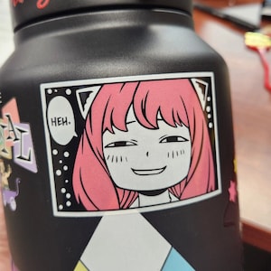 May include: A black water bottle with a sticker of a pink-haired anime character with cat ears. The sticker has a speech bubble that says "Heh."
