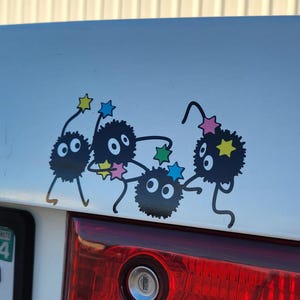 May include: A white car with a black and white sticker of five cartoon characters with stars on their heads. The characters are black with white eyes and are in a playful pose. The car has a Virginia license plate with the number ND205.