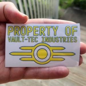 May include: A white sticker with the text "PROPERTY OF VAULT-TEC INDUSTRIES" in yellow and blue lettering. A yellow and blue Vault-Tec logo is below the text.