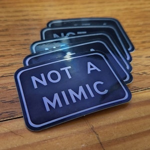 May include: A stack of black and white stickers with the text "NOT A MIMIC" in a white font.