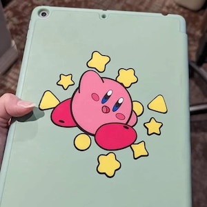 May include: A light green iPad case with a pink and red cartoon character with yellow stars and triangles around it.