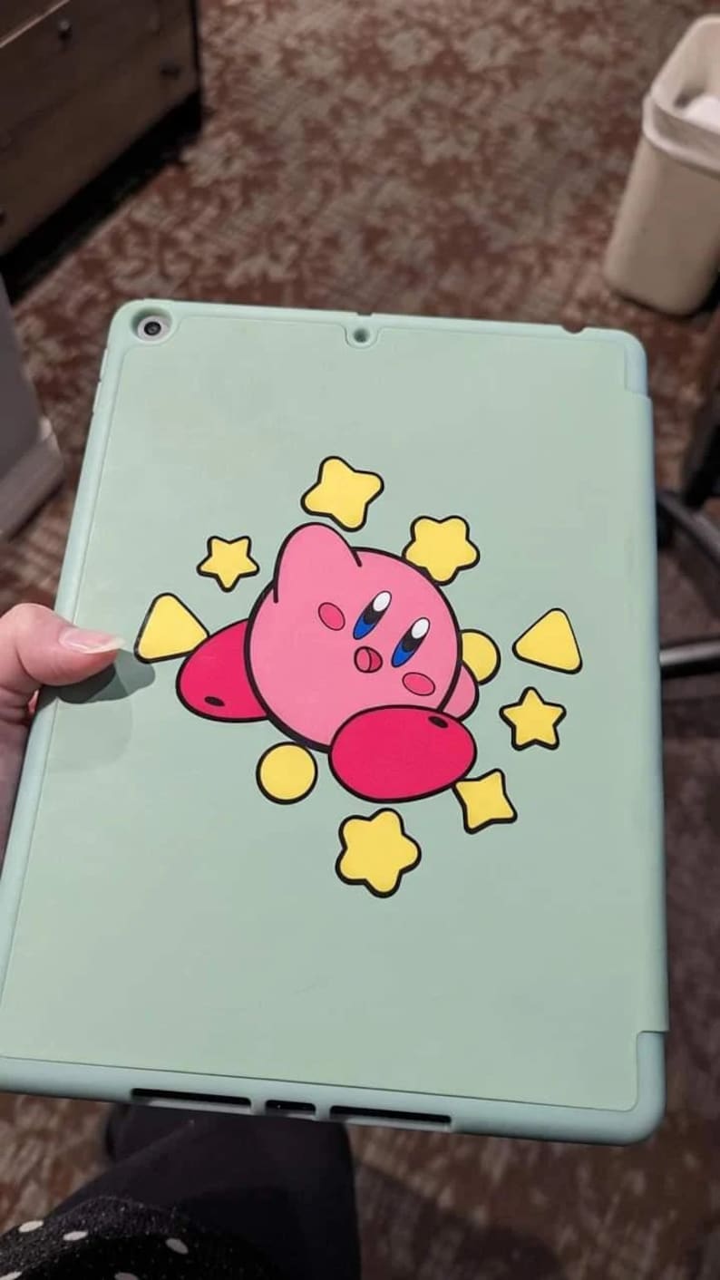 May include: A light green iPad case with a pink and red cartoon character with yellow stars and triangles around it.