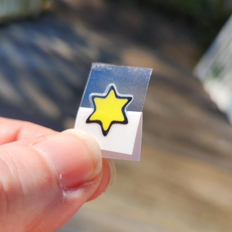 May include: A yellow six-pointed star sticker with a black outline on a white background.