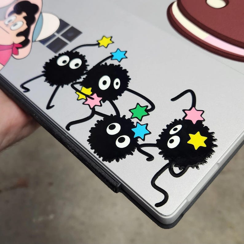 May include: A silver laptop with four black and white fuzzy round stickers with eyes and a string of colorful stars. The stickers are arranged in a line on the laptop.