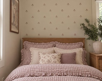Könnte beinhalten: Ein Bett mit einem mauve-weißen Vichy-Karo-Bettbezug mit Rüschenkanten, passenden Kissenbezügen, zwei cremefarbenen strukturierten Kissen, einem kleinen Kissen mit Blumenmuster, einem einfarbigen mauvefarbenen Kissen und einer cremefarbenen Strickdecke.