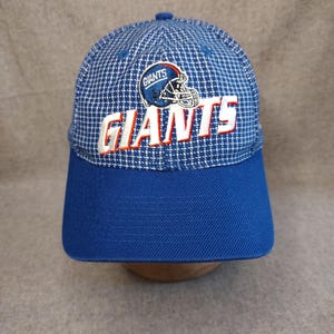 May include: A blue baseball cap featuring a white and blue checkered pattern on the crown. The front displays an embroidered New York Giants football helmet logo above the word GIANTS in white lettering with a red outline on a solid blue brim.